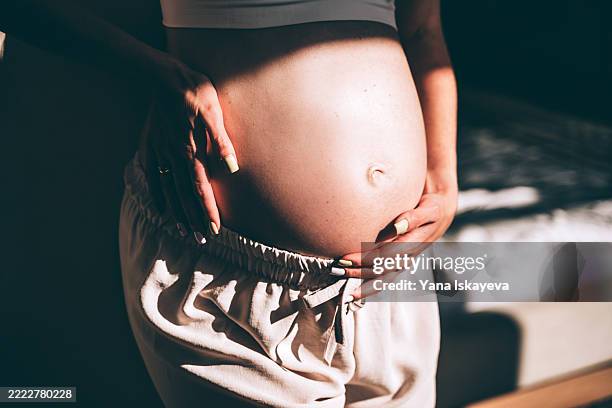 close-ip of a cute pregnant belly in natural light, gently held by mother's hands - embarazada fotografías e imágenes de stock