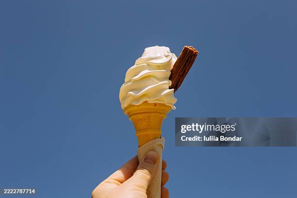 soft serve ice cream cone held against clear blue sky - mr whippy ice cream stock pictures, royalty-free photos & images