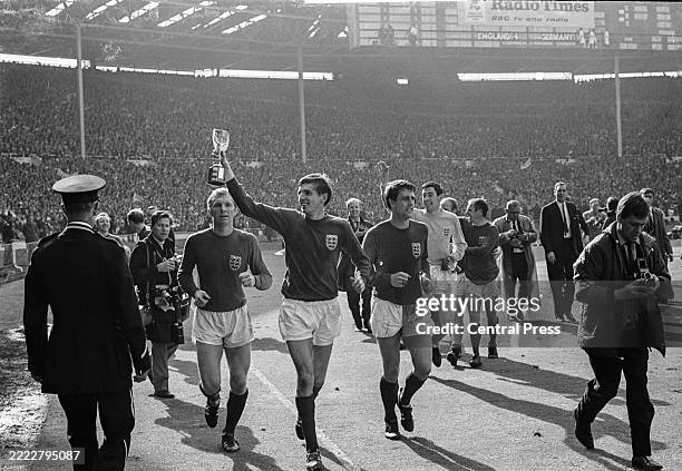 England soccer team captain, Bobby Moore, left, with strikers Martin Peters, holding World Cup trophy, and Geoff Hurst parading on the pitch after...
