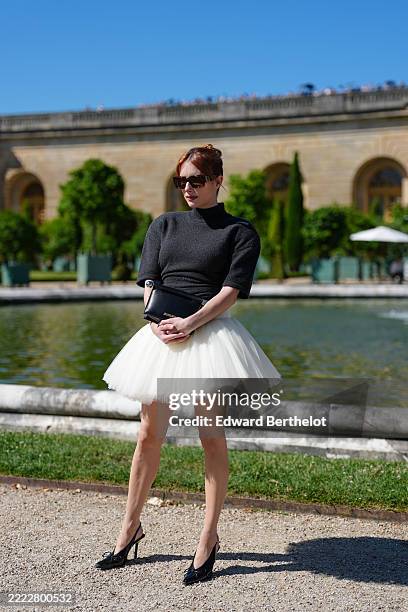 Emma Roberts wears a charcoal grey short-sleeved fitted knit top with a mock neck, tucked into a voluminous ivory tulle mini skirt, styled with...
