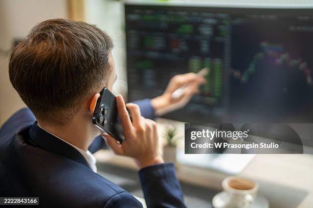 stockbroker analyzing charts on computer while talking on phone - trading floor stock pictures, royalty-free photos & images