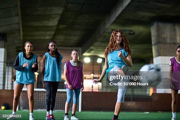 female football player kicking ball as team mates watch, ball in foreground - soccer skills stock pictures, royalty-free photos & images