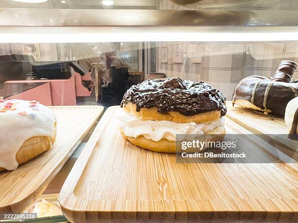 a donut with chocolate on top and cream in the middle on a tray at a bakery counter. bun, calories, unhealthy food, diabetes, unhealthy, fattening, fat, sweet, and fat. - glazed ham stock pictures, royalty-free photos & images