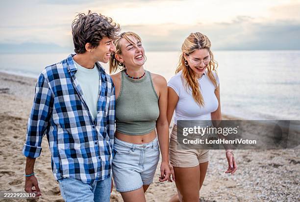 young friends walking and laughing on the beach at sunset - barefoot stock pictures, royalty-free photos & images