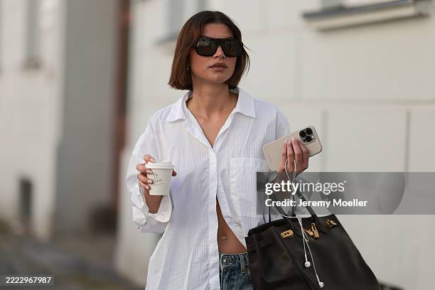 Sophia Geiss is seen wearing chunky silver hoop earrings, a silver nose ring, black aviator sunglasses from Vehla Eyewear, an oversized white...