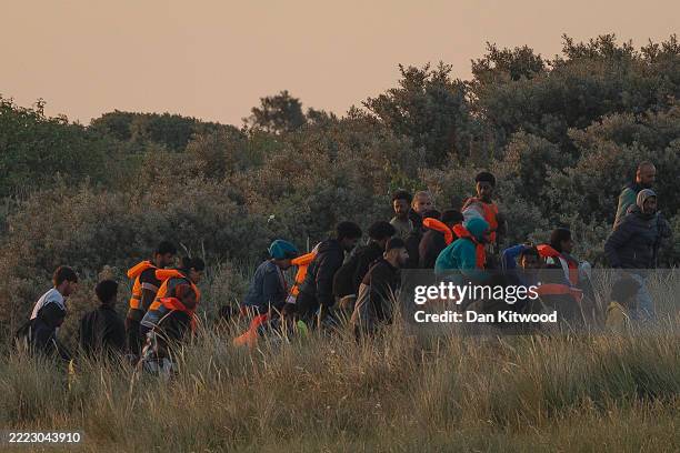 Large group of migrants emerge from the sand dunes before heading back in again as the police arrive on July 01, 2025 in Gravelines, France. French...
