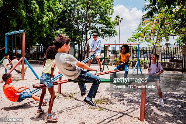 child friends playing on seesaw at public park - speeltuin stockfoto's en -beelden