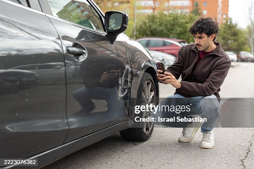 Young man photographing damage to car with smartphone after a car crash Young man photographing damage to car with smartphone after a car crash