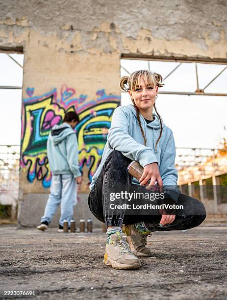junge graffiti-künstlerin posiert mit spraydose in verlassenem gebäude - straßenmaler stock-fotos und bilder