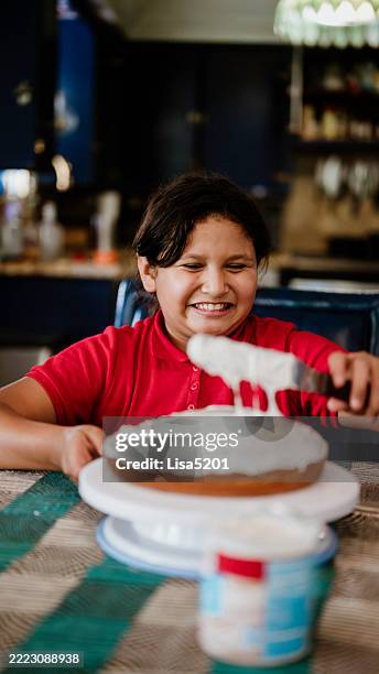 latina elementary age girl frosts and decorates a homemade cake at home - außerschulische aktivität stock-fotos und bilder