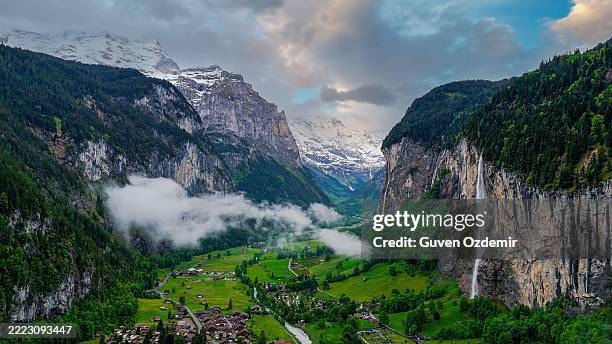 luftaufnahme des lauterbrunnentals in den schweizer alpen mit staubbachfällen, die von steilen klippen herabstürzen, traditionellen schweizer chalets auf saftig grünen wiesen und schneebedeckten berggipfeln im hintergrund, natur- und reisekonzept für d - tal stock-fotos und bilder