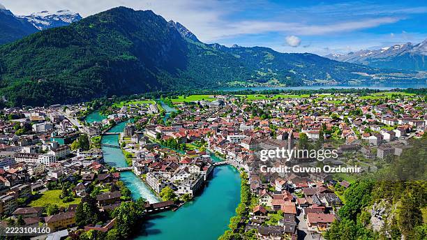 vue aérienne de la ville d’interlaken avec ses maisons au toit rouge, sa tour d’horloge historique et sa rivière turquoise entourée de montagnes verdoyantes, paysage urbain pittoresque entre le lac de thoune et le lac de brienz dans l’oberland ber - canton de berne photos et images de collection