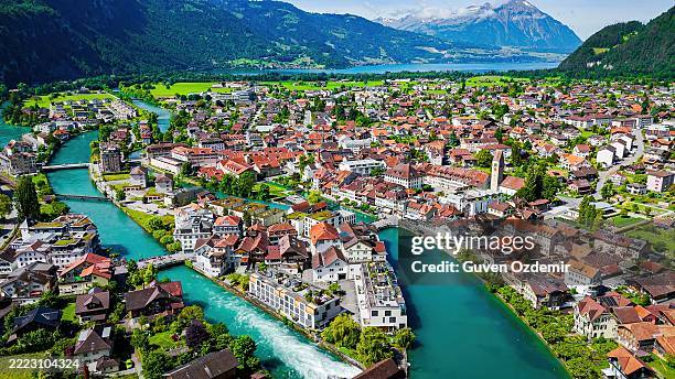 luftaufnahme der stadt interlaken mit roten häusern, historischem uhrturm und türkisfarbenem fluss, umgeben von saftig grünen bergen, malerische stadtlandschaft zwischen thunersee und brienzersee im berner oberland, schweiz - interlaken stock-fotos und bilder