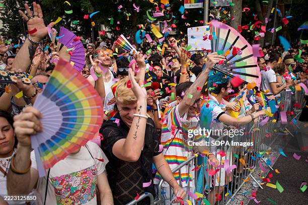 Attendees with rainbow color fans dance while papers are thrown at them, during the large Pride march that took place on Madrid's Paseo del Prado....