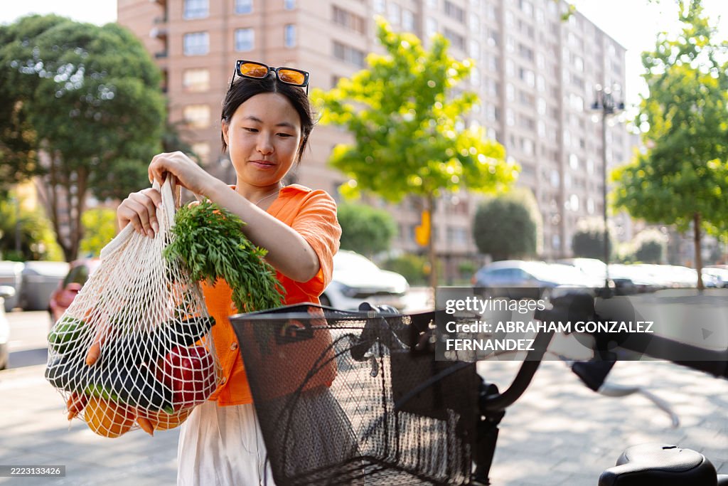 Mujer cargando productos de origen local en la cesta de la bicicleta, escena de estilo de vida verde urbano con verduras y hierbas frescas