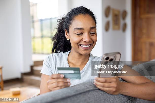 woman using her credit card while shopping online at home on her cell phone - subscription stock pictures, royalty-free photos & images