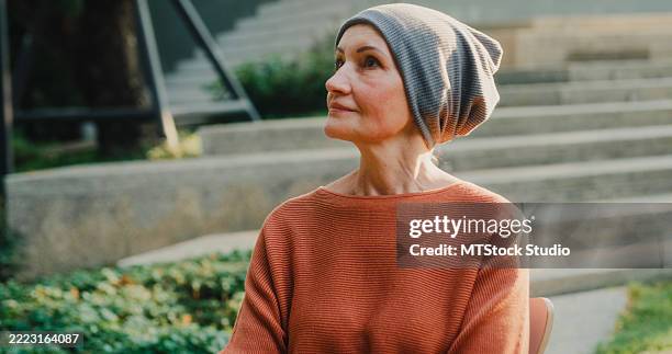 senior woman cancer patient with headscarf relaxing enjoy the warmth of sunlight and fresh air therapy recovery in the park. living with cancer concept. - leukemia stock pictures, royalty-free photos & images