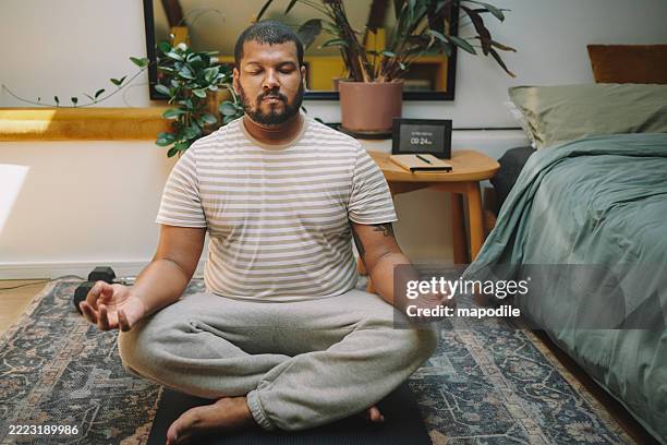 front view of man sitting on bedroom floor practicing meditation with his hands in gyan mudra - me time stock pictures, royalty-free photos & images