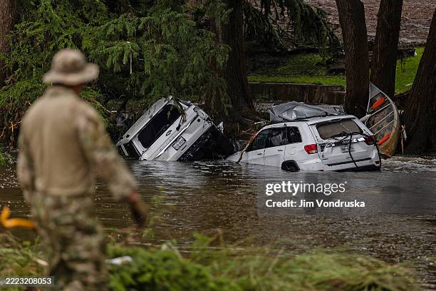 Vehicles sit submerged as a search and rescue worker looks through debris for any survivors or remains of people swept up in the flash flooding on...
