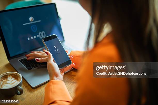 asian woman authorizing her identity by entering code from her phone to log in to her laptop. - identity theft stock pictures, royalty-free photos & images