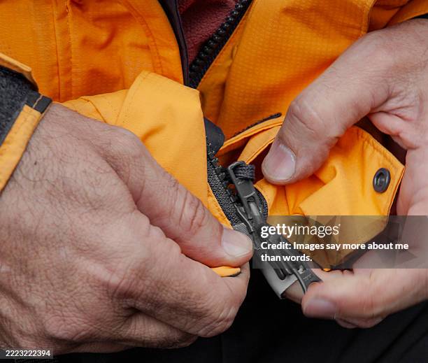 detail of hands trying to close the zipper of a jacket. - zipper stock pictures, royalty-free photos & images