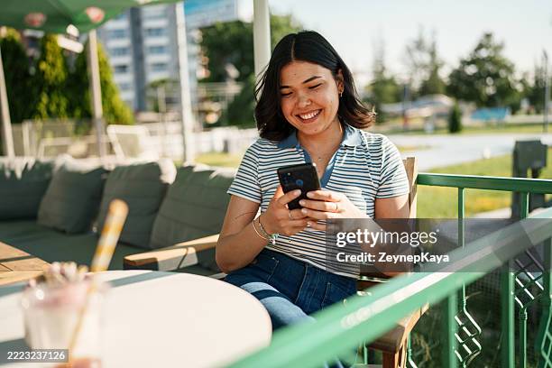 giovane donna che usa il telefono cellulare da sola in un caffè - social media marketing foto e immagini stock