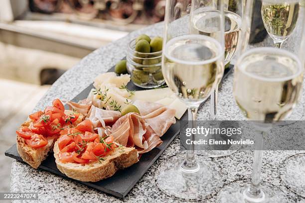 charcuterie plate with prosciutto crudo, salami, cheeses, green olives and tomato bruschetta with white wine, prosecco or champagnes, italian-style party or an aperitif with friends on the patio or on the terrace - cena con amigos fotografías e imágenes de stock