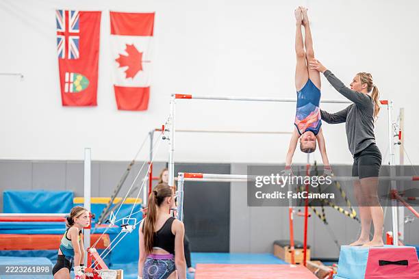 young gymnast practicing on bars with coach assistance in gymnastics training facility - gymnastics bar stock pictures, royalty-free photos & images