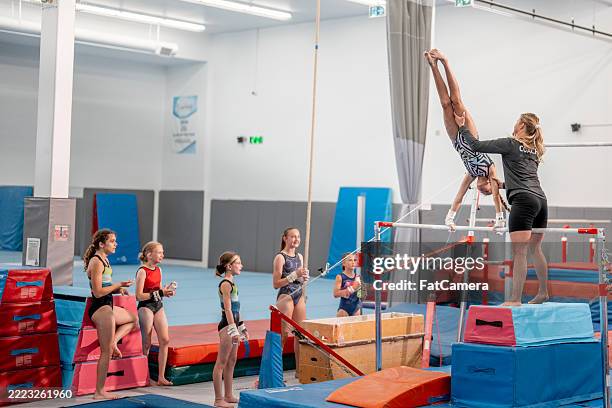 gymnastics coach supervising and training young athletes on uneven bars - turnen stockfoto's en -beelden
