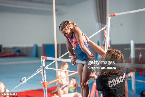 young gymnast practicing on bars with coach in training setting - gymnastics stock pictures, royalty-free photos & images