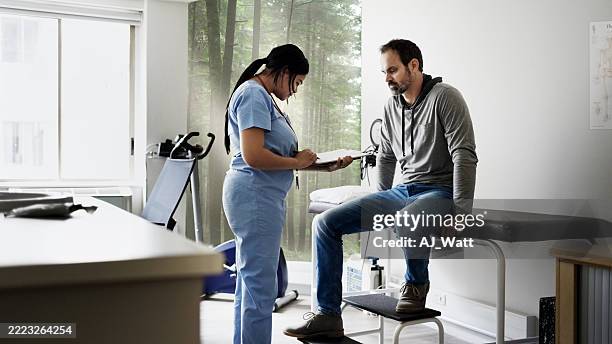 medical professional writing on clipboard while patient sits on examination table - examination table stock pictures, royalty-free photos & images