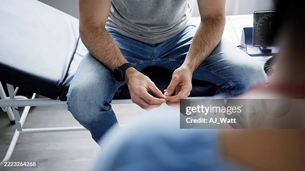 patient masculin assis sur la table d’examen dans une clinique - blouse dexamen médical photos et images de collection