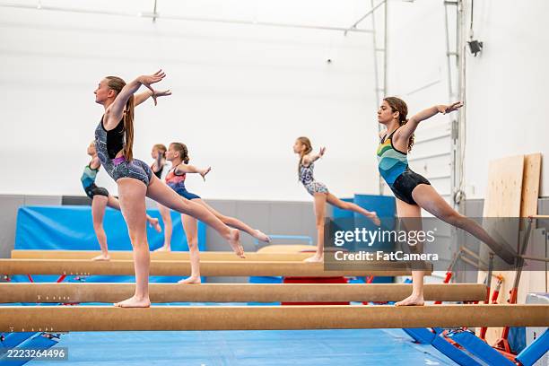 group of girls practicing gymnastics on balance beam in indoor training facility - turnen stockfoto's en -beelden