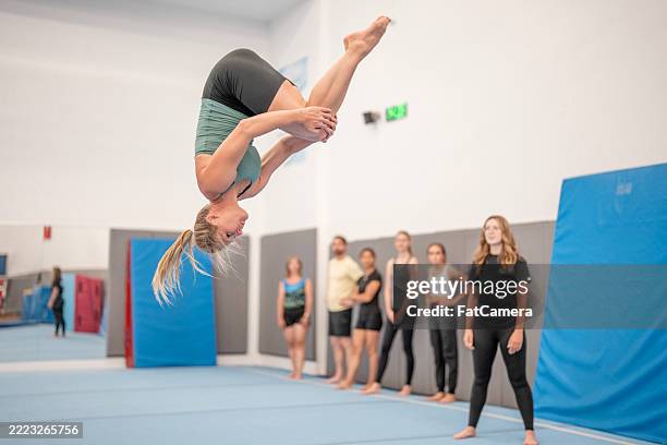 gymnast performing flip in training facility with observing group - acrobatiek stockfoto's en -beelden