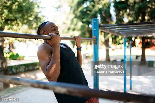 young determined athlete doing pull-ups on a horizontal bar in a park - doing pull ups stock pictures, royalty-free photos & images