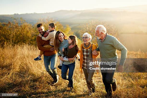 feliz familia multigeneracional corriendo en un día de otoño en una colina. - familia multigeneracional fotografías e imágenes de stock