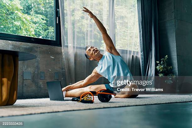 senior male works out at home while watching a laptop computer - anziani attivi foto e immagini stock