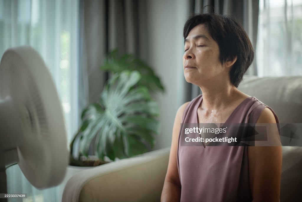 Mature woman experiencing hot flash while sitting on sofa.