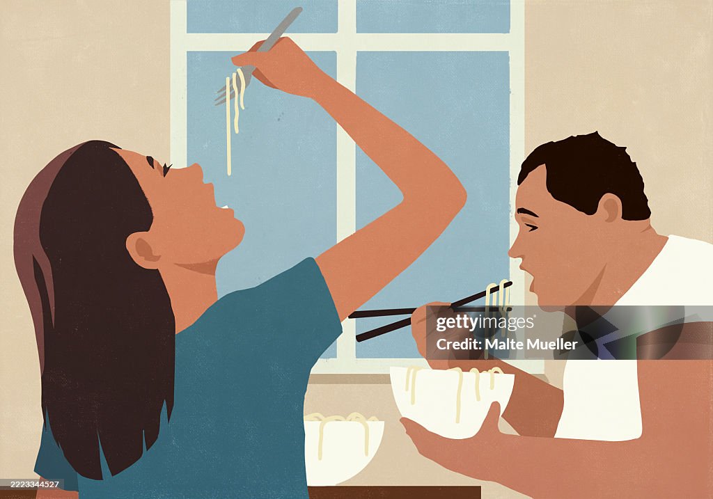 Couple eating pho noodles from bowls with fork and chopsticks at home