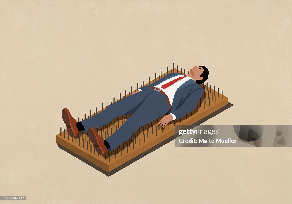 Businessman laying on bed of nails against beige background