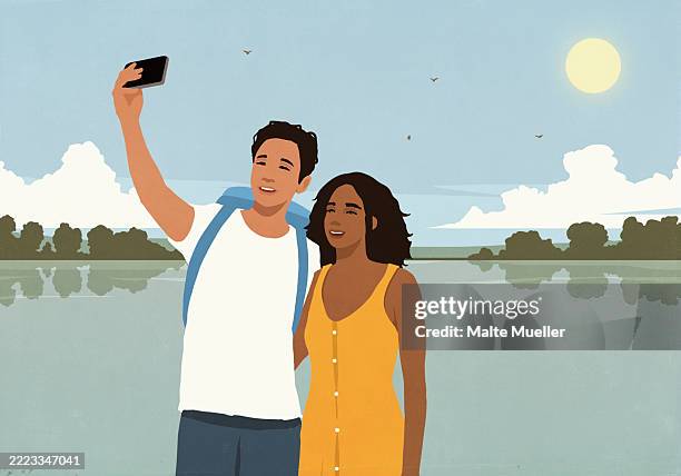 happy young multiracial couple taking a selfie with smart phone on vacation at sunny summer lake - selfie stock illustrations
