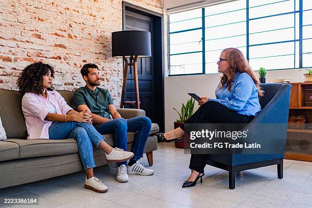 young couple talking with psychotherapist during couple therapy session at clinic - terapia de pareja fotografías e imágenes de stock