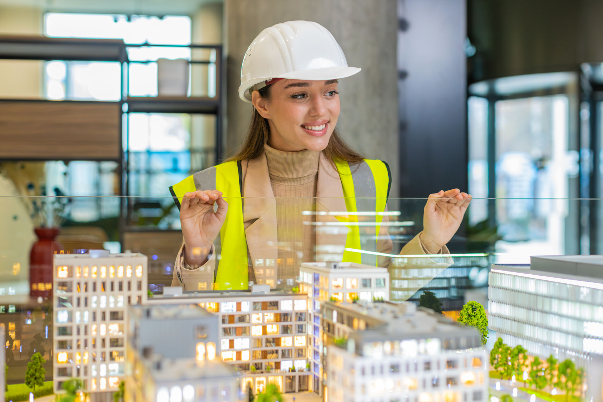 Confident young female architect in hardhat analyzing office complex architectural model in office Confident young female architect in hardhat analyzing office complex architectural model in office