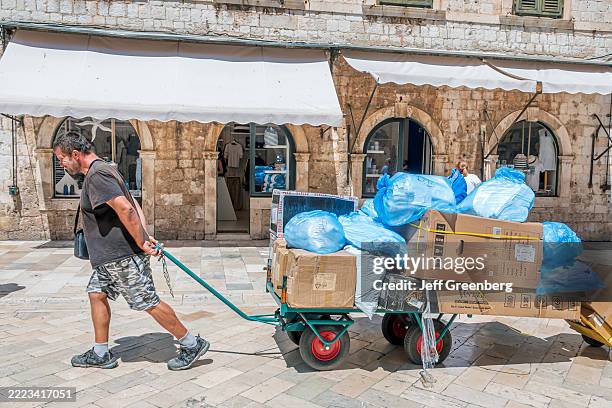 Dubrovnik, Croatia, Walled City, Stradun Placa, main street, man worker pulling cart, loaded plastic trash litter bags boxes.