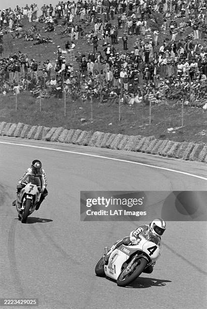 In front of a hillside half filled with spectators, Johnny Cecotto leans into a left hander on his Yamaha YZR500, followed by Barry Sheene on his...