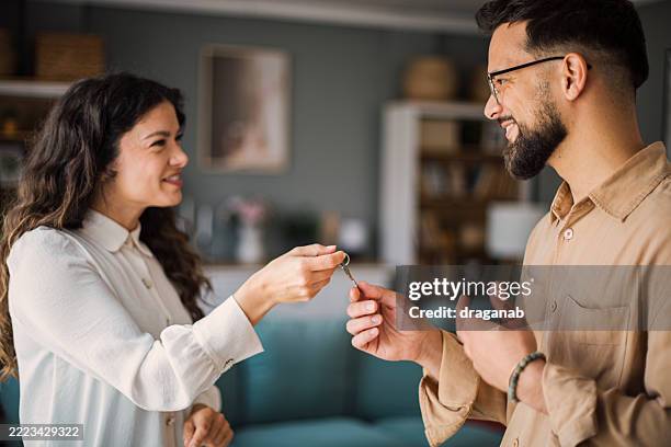 smiling couple exchanging house keys indoors - uitwisselen stockfoto's en -beelden