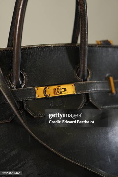 Close-up detail of Jane Birkin’s original Hermès Birkin bag in black leather, showing oxidized gold-tone hardware, visible patina, and the embossed...