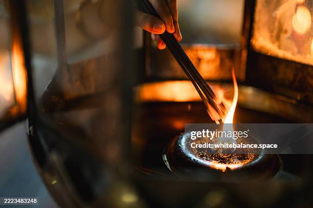 close-up shot of hand holding a glowing candle, gently lighting a flame in a traditional oil lamp at a sacred shrine - religious offering stock pictures, royalty-free photos & images