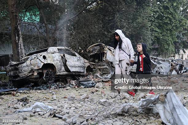 Mother leads her child near burned-out cars and the rubble of a 5-story residential building in Solomyanskyi district heavily damaged by a Russian...