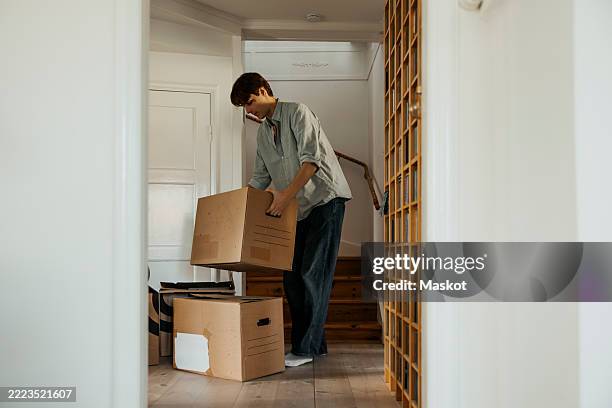 full length of young man picking up cardboard boxes in new home - umzug stock-fotos und bilder